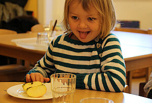 Ein Mädchen sitzt am Tisch, vor sich auf dem Teller ein aufgeschnittener Apfel.