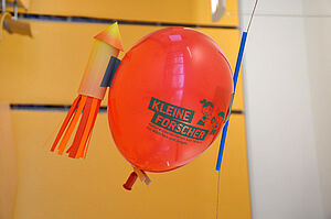 Lufballon mit einer Papierrakete dekoriert hängt an einer Schnur.