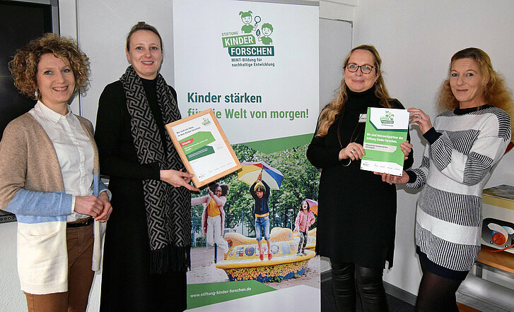 Kerstin Tote und Christina Mersch von der Stiftung Kinder forschen und die neuen Koordinatorinnen in Salzgitter, Antje Behre und Kristina Wojna, halten die Plaketten in die Kamera.