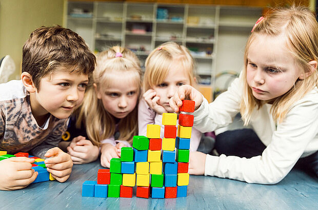 Grundschulkinder vor einem bunten Stapel mit Bausteinen
