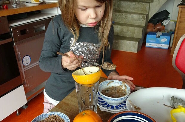 Mädchen befüllt eine leere Orangenschalenhälfte mit Vogelfutter.