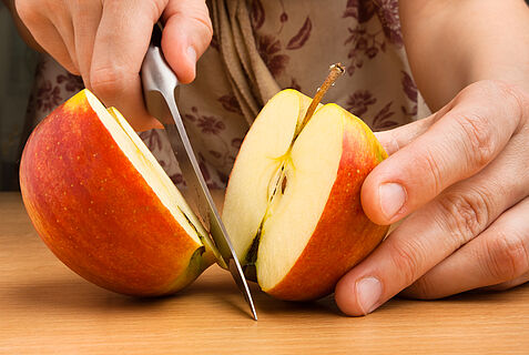 Nahaufnahme von zwei Händen, die einen Apfel schneiden