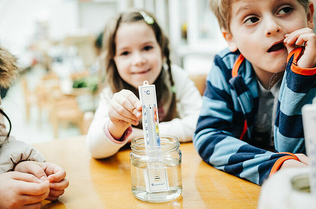 Ein Mädchen hält ein Thermometer in ein Wasserglas.