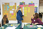 Drei Personen entwickeln am Board mit geschriebenen Karten und Post-its neue Ideen