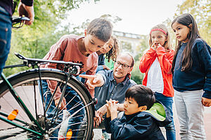Zwei Jungen und drei Mädchen stehen mit einer Lehrkraft um ein Fahrrad herum und sprechen über das Rücklicht.