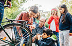 Zwei Jungen und drei Mädchen stehen mit einer Lehrkraft um ein Fahrrad herum und sprechen über das Rücklicht.