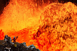 Eine Frau mit Kamera vor brodelnder Lava.
