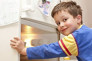 Junge guckt freudig in einen geöffneten Kühlschrank.