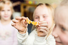 Ein Kind hält ein Stück Mandarine zwischen den Fingern