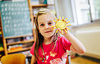Ein Mädchen im Grundschulalter hält eine selbstgebastelte Sonne hoch.