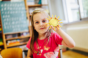 Ein Mädchen im Grundschulalter hält eine selbstgebastelte Sonne hoch.