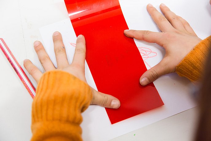 Ein Kind verdeckt Kritzeleien mit einer roten Farbfolie und entdeckt Buchstaben