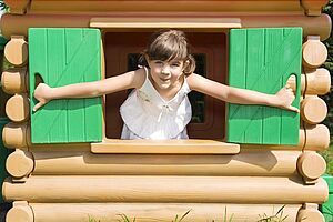 Lachendes Mädchen schaut aus dem Fenster einer Holzhütte
