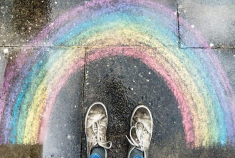 Zwei Füße stehen vor einem Regenbogen aus Kreide