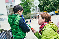Eine Frau kniet neben einem Kind und hält ihm eine Lupe hin.