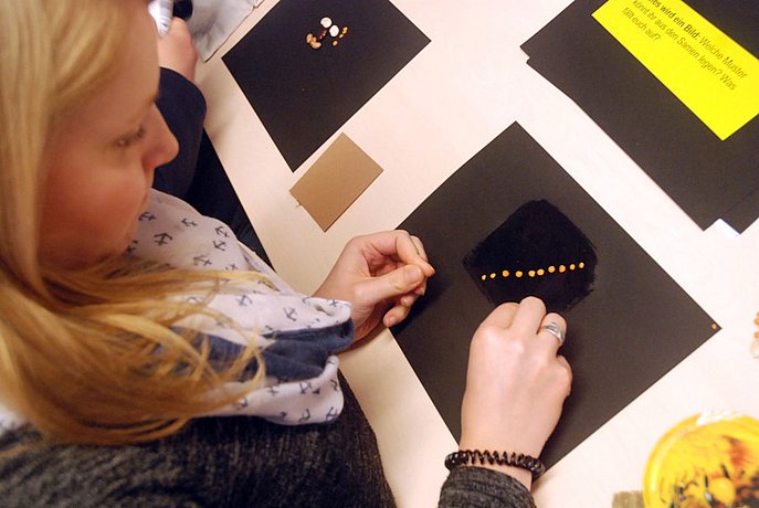 Eine Frau legt ein Muster aus Linsen auf schwarzes Papier