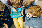Kinder sitzen um ein Tablet und schauen auf das Display.