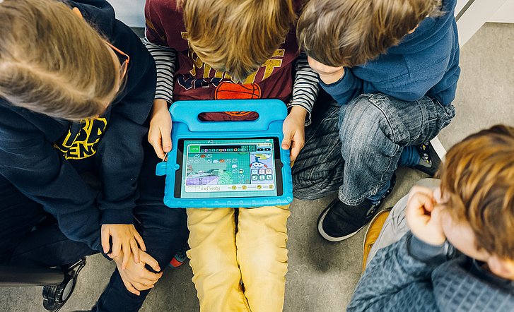 Vier Kinder schauen gemeinsam etwas auf einem Tablet an.