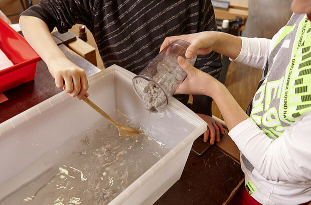 Kind füllt Ppaierbrei in Box mit Wasser