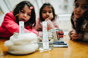 Drei Mädchen messen mit Thermometern die Wassertemperatur in drei Gefäßen.
