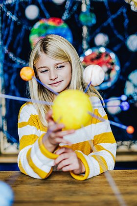Ein Mädchen hält das Model eines gelben Planeten in der Hand.