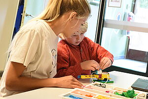 Eine Erzieherin und ein Kind bauen gemeinsam an einem Tisch Lego.