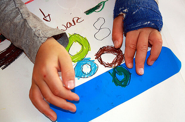 Ein Kind legt eine blaue Folie auf ein gemaltes Bild