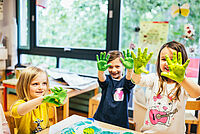 Drei Kinder halten ihre mit grüner Farbe bemalten Hände in die Kamera