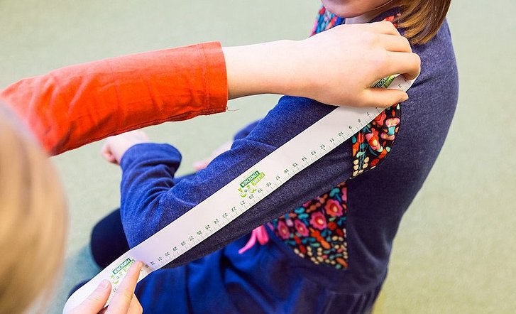 Ein Kind misst den Arm eines anderen Kindes mit dem Lineal.