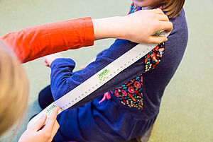Ein Kind misst den Arm eines anderen Kindes mit Hilfe eines Lineals.