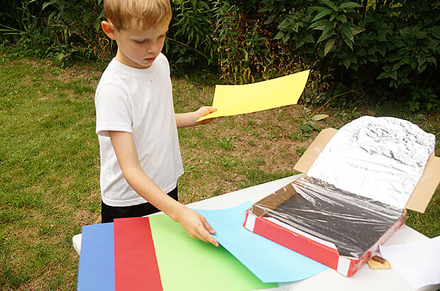 Ein Junge überlegt, welches farbige Papier er in seinen Solarofen stecken könnte