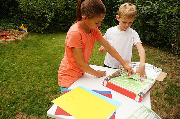 Ein Mädchen und ein Junge schieben ein grünes Stück Papier in ihren Solarofen