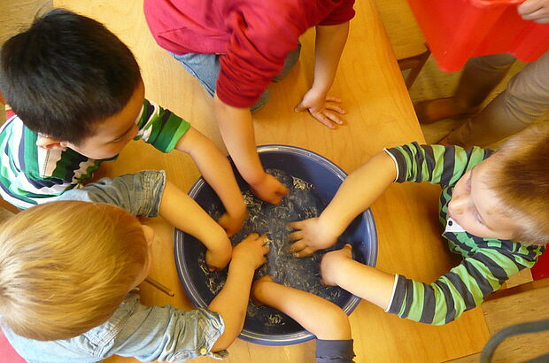 Fünf Kinder halten ihre Hände in einen Bottich voll Wasser