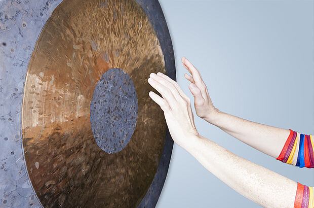 Zwei Hände halten vor einem großen Gong aus Metall.