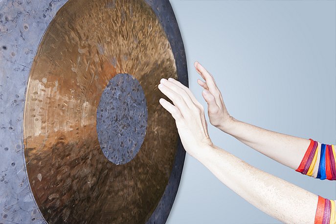 Zwei Hände halten vor einem großen Gong aus Metall.