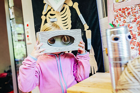 ein Kind schaut durch eine selbst gebastelte Maske