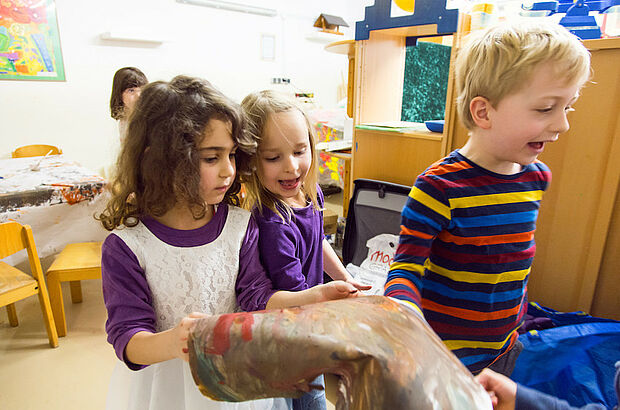 Mehrere Kinder halten ein selbstgemaltes Bild in der Hand, das ein Gemisch aus den verschiedensten Farben ist