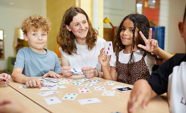 Ein Mädchen hält drei Finger hoch, passend zu der Anzahl der Symbole auf einer Spielkarte.