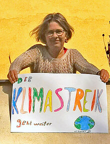Frau hält gemaltes buntes Plakat in der Hand: "Der Klimastreik geht weiter!"