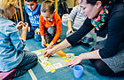 Kinder legen zusammen mit einer Erzieherin Karten auf den Boden