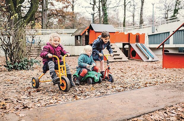 Drei Kinder spielen mit Fahrzeugen auf einem Spielplatz