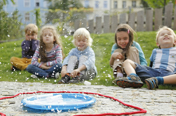 Fünf Kinder sitzen um einen Teller von dem aus Wasser spritzt.