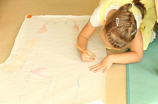 Mädchen malt sich selbst in Lebensgröße als Umrisszeichnung auf Papier.