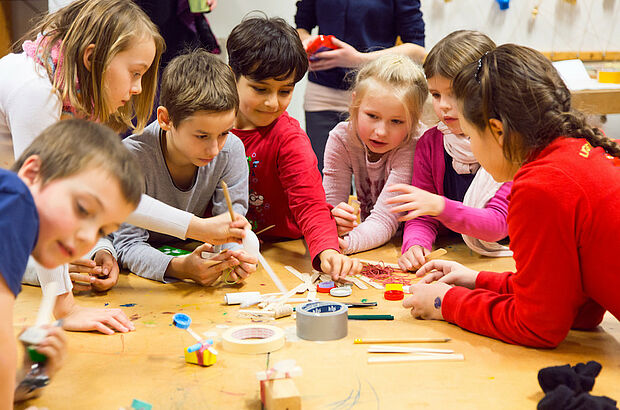 Mehrere Kinder greifen nach Materialien auf einem Tisch