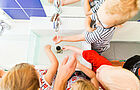 Kinder stehen um ein Waschbecken herum, das Wasser läuft.