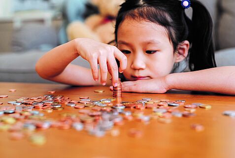 Ein Mädchen zählt Münzen, die auf einem Tisch liegen