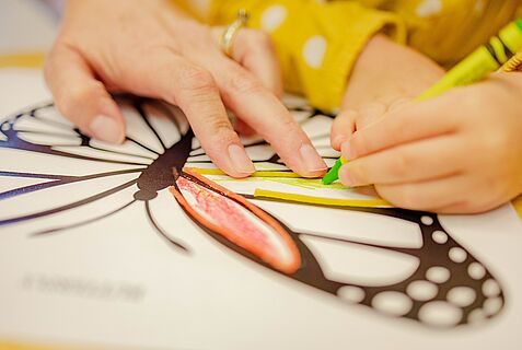 Kinderhand malt Schmetterlingvorlage auf Papier aus
