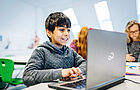 Ein Junge sitzt freudig vor einem Laptop und tippt etwas ein