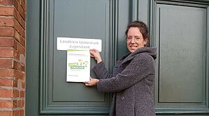 Eine Frau hält eine Plakette "Haus der kleinen Forscher" an eine Tür.