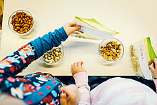 Ein Kind reicht einem weiteren eine Tüte weiter, um sie mit Nüssen zu befüllen.